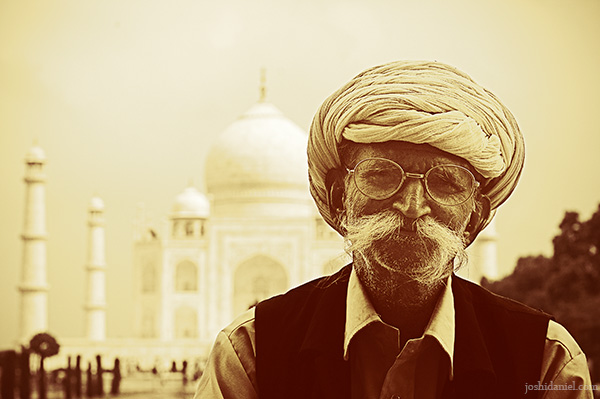 Portrait of a happy old man with turban and a long mustache sitting in front of Taj Mahal