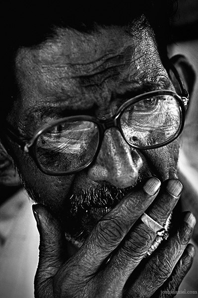 Black and white portrait of an old man with spectacles smoking beedi
