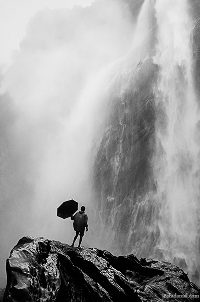 A man with umbrella standing under a waterfall
