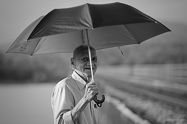 Black and white portrait of a beaming old man holding an umbrella from Kumta in Karnataka