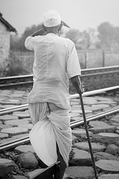 Black and white photograph of an old Maharashtrian man walking across railway tracks in Pune, Maharashtra