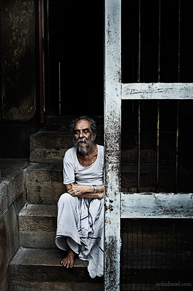 Portrait of an old man sitting on a staircase behind a door in Trivandrum, Kerala