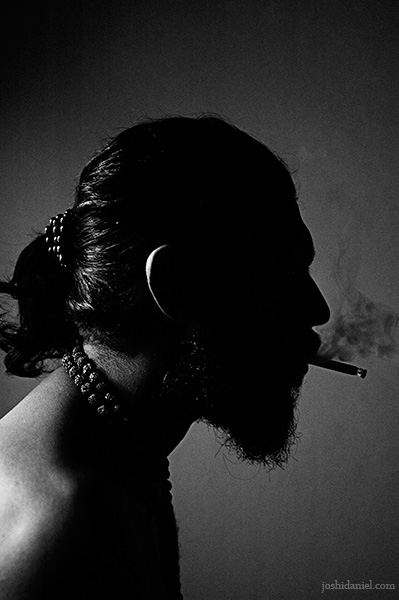 Black and white portrait of Abilash Thankan smoking in darkness