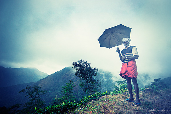 Old man standing on Ponmudi hills, holding an umbrella