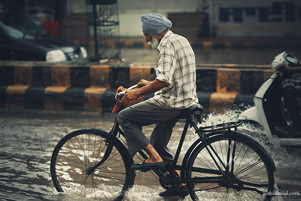 A turbaned old man cycling away on a flooded road during the rains in Amritsar, Punjab