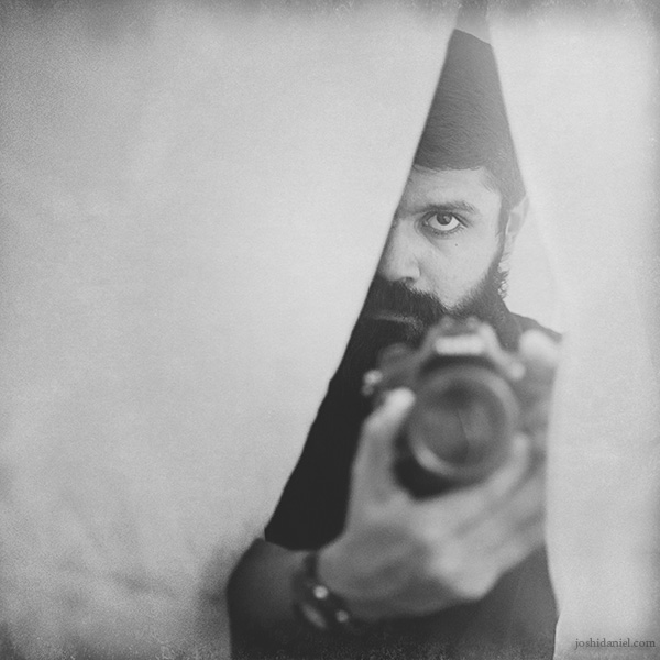 Black and white self-portrait of joshi daniel hiding behind a curtain