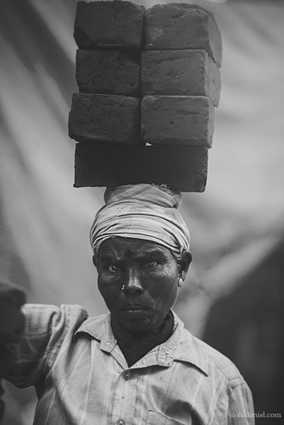 Black and white portrait of a female labourer in Chennai, India, carrying a large set of bricks on her head