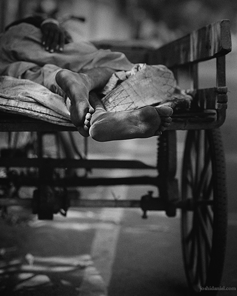 Black and white photo of the feet of a man sleeping on a pushcart in Chennai, India