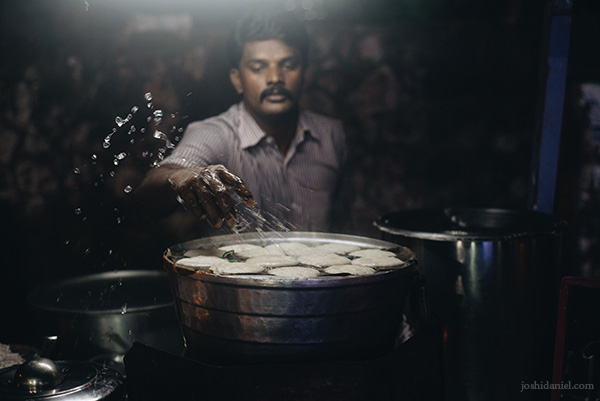 Portrait of an idli vendor splashing water over cooked idlis in Chennai