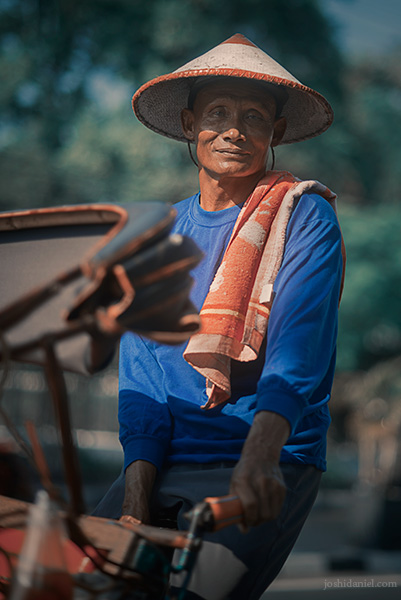 Portrait of a smiling becak (rickshaw) driver wearing a straw hat in Yogyakarta, Indonesia