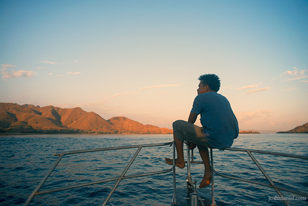 Man sitting on the bow of a boat sailing from Pink Beach, Indonesia