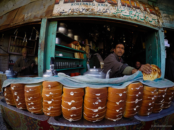 A tea seller standing behind a full stack of buttered bread in a tea shop in Kokernag, Jammu and Kashmir