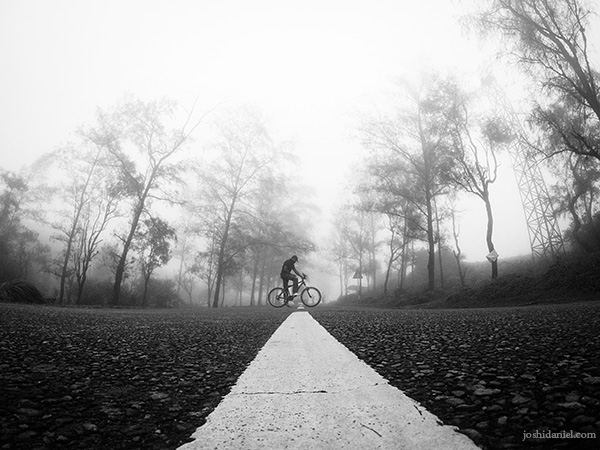 Black and white self-portrait of joshi daniel on a bicycle in the middle of the road in Ponmudi in Trivandrum, Kerala