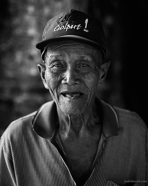 Black and white portrait of a smiling old man at the Banyan tree temple at Senggarang Village, Indonesia