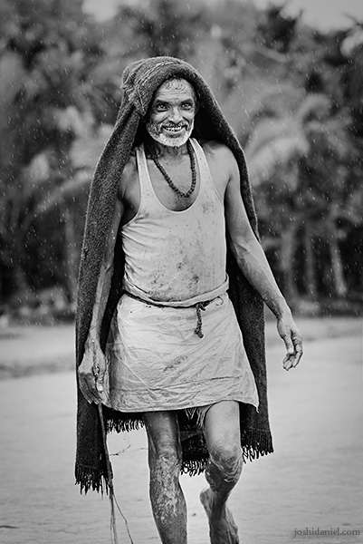 A smiling farmer in Karnataka, India shielding himself from the rain