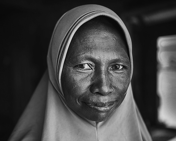 A 28mm wide angle black and white portrait of a smiling hijabi woman from Rainbow Village, Tual, Maluku, Indonesia