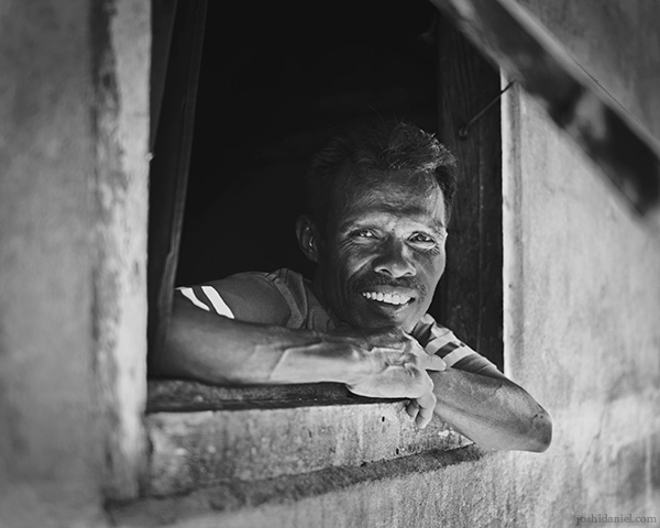 A 28mm wide angle black and white portrait of a man curiously looking out of a window in Tual, Maluku, Indonesia