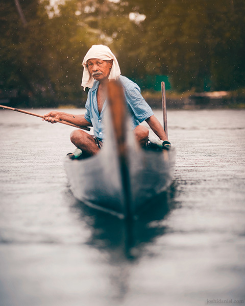 An old man fishing out of his boat on a rainy day in Alappuzha, Kerala, India