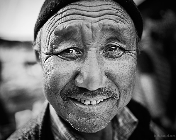 Creased A 28mm wide angle black and white portrait of smiling Dorjee, the owner of a dhaba in Batal, Spiti Valley, Himachal Pradesh, India