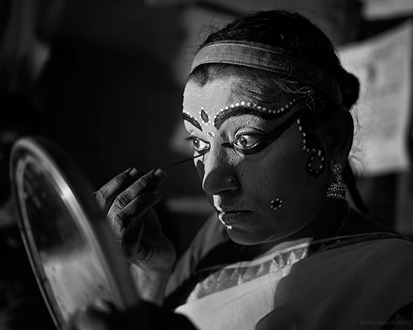 A 28mm wide angle black and white portrait of Nangiarkoothu artist Margi Usha doing make-up in Trivandrum, Kerala, India